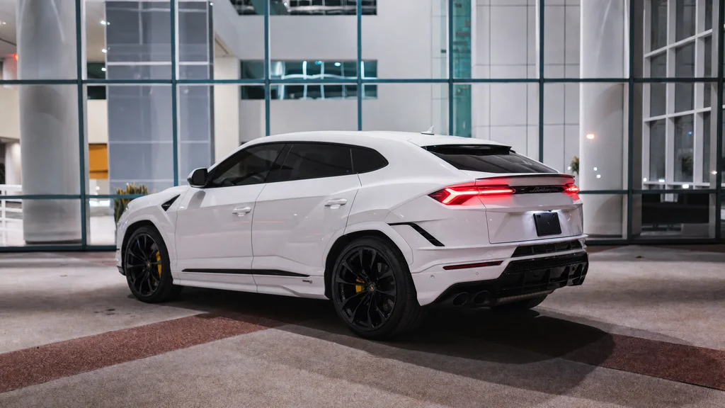 White Lamborghini Urus S outside a glass-fronted building, rear three-quarter view